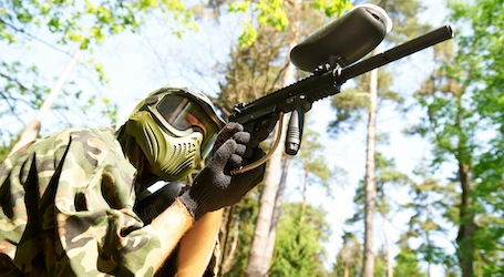 man in the bush shooting paintball gun with army outfit and face mask